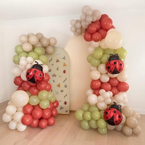 May include: A whimsical balloon arch and column set in red, white, green, and beige. The arch and column are decorated with ladybug-shaped balloons. The backdrop features a light beige arch with insect illustrations.