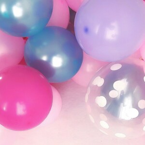 Pode incluir: Uma cole&ccedil;&atilde;o de bal&otilde;es redondos em v&aacute;rias cores, incluindo rosa brilhante, rosa claro, lavanda e azul met&aacute;lico. Um bal&atilde;o transparente apresenta um padr&atilde;o de bolinhas brancas. Os bal&otilde;es est&atilde;o agrupados, criando uma exibi&ccedil;&atilde;o vibrante.