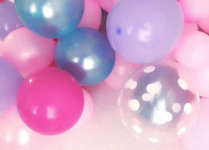 Pode incluir: Uma cole&ccedil;&atilde;o de bal&otilde;es redondos em v&aacute;rias cores, incluindo rosa brilhante, rosa claro, lavanda e azul met&aacute;lico. Um bal&atilde;o transparente apresenta um padr&atilde;o de bolinhas brancas. Os bal&otilde;es est&atilde;o agrupados, criando uma exibi&ccedil;&atilde;o vibrante.
