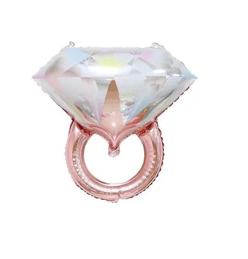 May include: A diamond ring shaped balloon featuring a large, iridescent, multifaceted gemstone top with a reflective, holographic finish and a metallic rose gold band. The design mimics the appearance of a faceted diamond set on a circular ring.