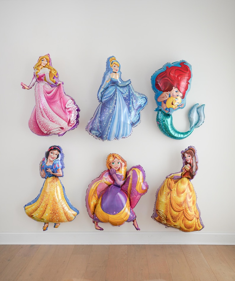 Pu&ograve; includere: Una collezione di sei palloncini in alluminio a forma di varie principesse animate. I palloncini raffigurano personaggi con abiti rosa, blu, gialli e viola, insieme a una sirena con capelli rossi e coda verde, tutti con finiture lucide.
