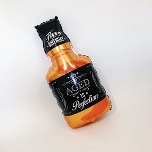 May include: A gold and black foil balloon shaped like a bottle of whisky. The balloon has the text "Happy Birthday" and "Aged to Perfection" printed on it.