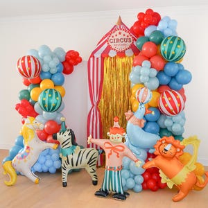 K&ouml;nnte beinhalten: Eine Zirkus-Themen-Ballonbogen mit roten, blauen, gr&uuml;nen und gelben Ballons. Aufblasbare Zirkusfiguren wie Zebra, L&ouml;we, Clown und Seehund. Eine Zirkuszelt-Kulisse mit goldenen Fransen.