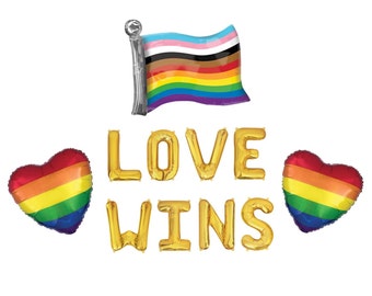 May include: A set of foil balloons including a flag balloon with horizontal stripes in light blue, pink, white, brown, black, red, orange, yellow, green, and purple. Gold letter balloons spell out LOVE WINS, flanked by two rainbow heart balloons.