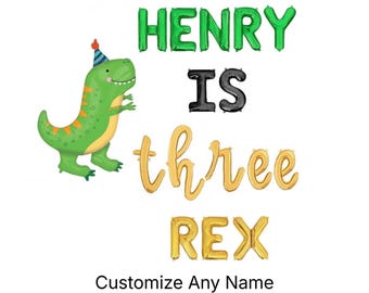 May include: A graphic design featuring a green cartoon dinosaur wearing a blue and red party hat. The text reads HENRY IS three REX in a mix of green, black, and gold balloon-style letters. Below the design, the text reads Customize Any Name.