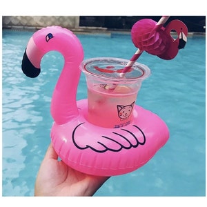 May include: Pink inflatable flamingo drink holder with a clear plastic cup and a pink and white striped straw. The flamingo has a black eye and a black beak. The cup has a cartoon cat with a bow tie on it.