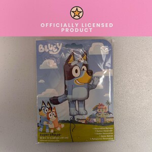 Op de afbeelding: Een decoratieve ballon met Bluey-thema in de originele plastic verpakking. De verpakking bevat het Bluey-logo, een illustratie van Bluey en Bingo, en een huis. De tekst vermeldt 60 cm x 81 cm en Officially Licensed Product.