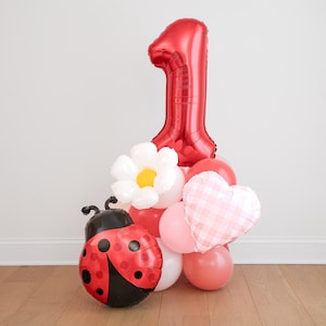 May include: A festive balloon arrangement for a first birthday celebration. It features a large red number 1 balloon, a ladybug balloon, a white flower balloon, a pink heart balloon, and several other pink and red balloons.