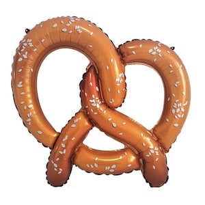 May include: A large, inflatable pretzel balloon in a golden-brown color, with white sesame seed-like details. The balloon is shaped like a traditional pretzel, perfect for a party or event.