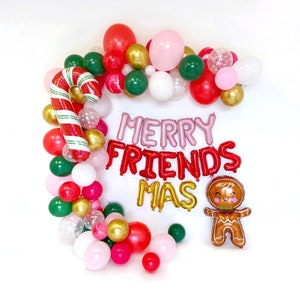 May include: A festive balloon arch featuring red, green, gold, white, and pink balloons, a large candy cane balloon, and a gingerbread man balloon. The text MERRY FRIENDS MAS is spelled out in pink, red, and gold foil letter balloons.