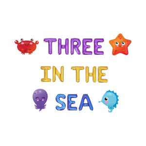 May include: A set of foil balloons spelling "THREE IN THE SEA", with sea creature illustrations. The balloons are purple, gold, and blue, with a crab, starfish, octopus, and seahorse.