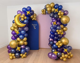 Könnte beinhalten: Zwei Ballonbögen, einer mit blauem Hintergrund und der andere mit rosa Hintergrund. Die Bögen sind mit goldenen, lila und blauen Luftballons geschmückt, darunter stern- und mondförmige Folienballons. Der blaue Hintergrund hat den Text "Capricorn Sun" und ein Steinbock-Symbol.