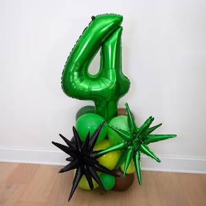 May include: A green number 4 foil balloon centerpiece with a cluster of green, yellow, and black star-shaped balloons. The balloons are arranged on a wooden base, perfect for a birthday celebration.