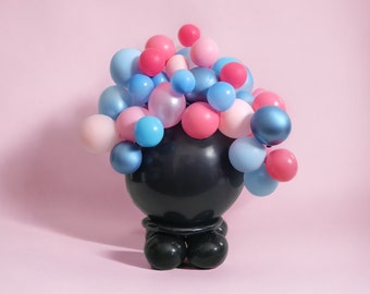 Puede incluir: Un soporte de globos negro con un grupo de globos rosas, azules y azul claro en la parte superior. El soporte tiene tres patas y está hecho de plástico negro.