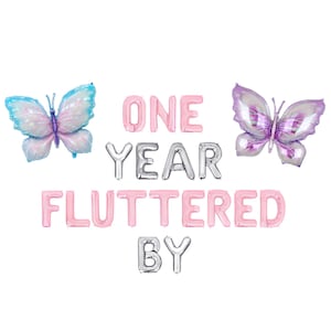 May include: A festive arrangement of foil balloons spelling "ONE YEAR FLUTTERED BY" in pink and silver. Two butterfly-shaped balloons in blue and purple flank the text, creating a celebratory theme.