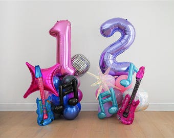 May include: A festive balloon arrangement spelling out the number 12. The arrangement includes pink and purple number balloons, star-shaped balloons, musical note balloons, and guitar-shaped balloons. A disco ball balloon adds a touch of sparkle.