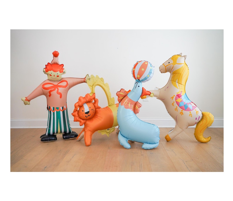 May include: A collection of circus-themed foil balloons. Includes a clown, a lion, a seal balancing a ball, and a horse. The balloons are brightly colored with details like stripes, patterns, and a yellow mane.