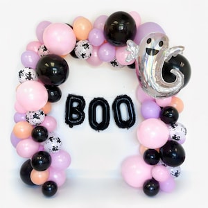 May include: A Halloween balloon garland with pink, purple, and black balloons. The garland spells out "BOO" with black balloons. There is a silver ghost balloon in the center of the garland.