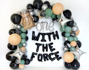 May include: A balloon arch with black, green, beige, and silver balloons. The arch is decorated with a small Yoda figure and the text "one with the force".