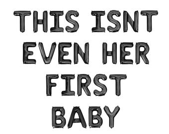 May include: Black foil balloons spelling out "THIS ISN'T EVEN HER FIRST BABY" against a white background. The balloons are arranged in three rows, with the words centered.