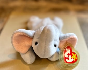 May include: A gray plush elephant toy with pink ears and a Ty tag. The tag is a red heart with a white star and the word "Ty" in white.