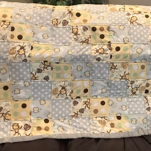 May include: A patchwork baby quilt with a monkey theme. The quilt is made of various fabrics in shades of gray, yellow, brown, and green. The fabric features a repeating pattern of monkeys, leaves, and polka dots.