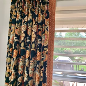 May include: Dark floral patterned curtains with a black background, featuring orange, gold, and green botanical designs. The curtains are pleated and hung on a silver rod. A decorative trim in shades of red and orange borders the edge.