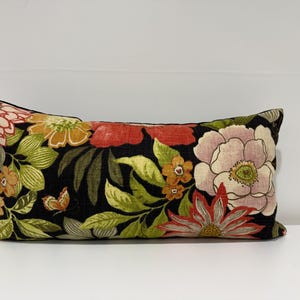 May include: Rectangular decorative pillow with a black background and a vibrant floral pattern. The design features large flowers in shades of pink, orange, and red, with green leaves and a small butterfly.