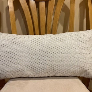 May include: A white lumbar pillow with a subtle gray geometric pattern. The pillow is on a wooden chair.