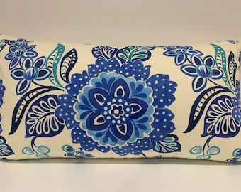 May include: A white rectangular pillow with a blue and teal floral pattern. The pillow features a large blue flower with white dots in the center.
