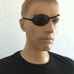 May include: A black leather eye patch with an elastic strap. The patch is worn over the right eye.
