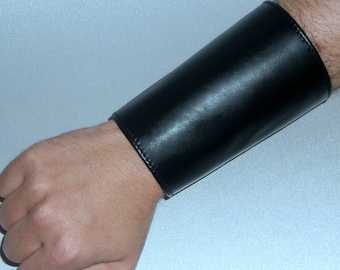 May include: A black leather cuff bracelet worn on a person's wrist.