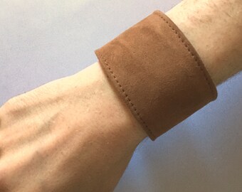 May include: A brown suede bracelet with stitching around the edges.