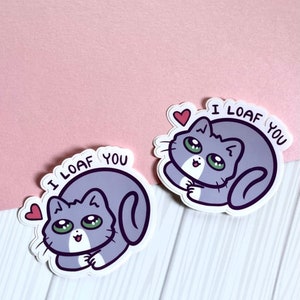 May include: Two stickers featuring a cartoon cat with the text "I LOAF YOU" and a heart. The cat is gray with white accents and is curled up in a loaf shape.