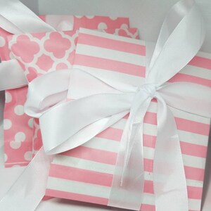 Puede incluir: Dos bolsas de regalo rosas con lunares blancos y un patr&oacute;n geom&eacute;trico blanco. Las bolsas est&aacute;n atadas con una cinta de sat&eacute;n blanca.