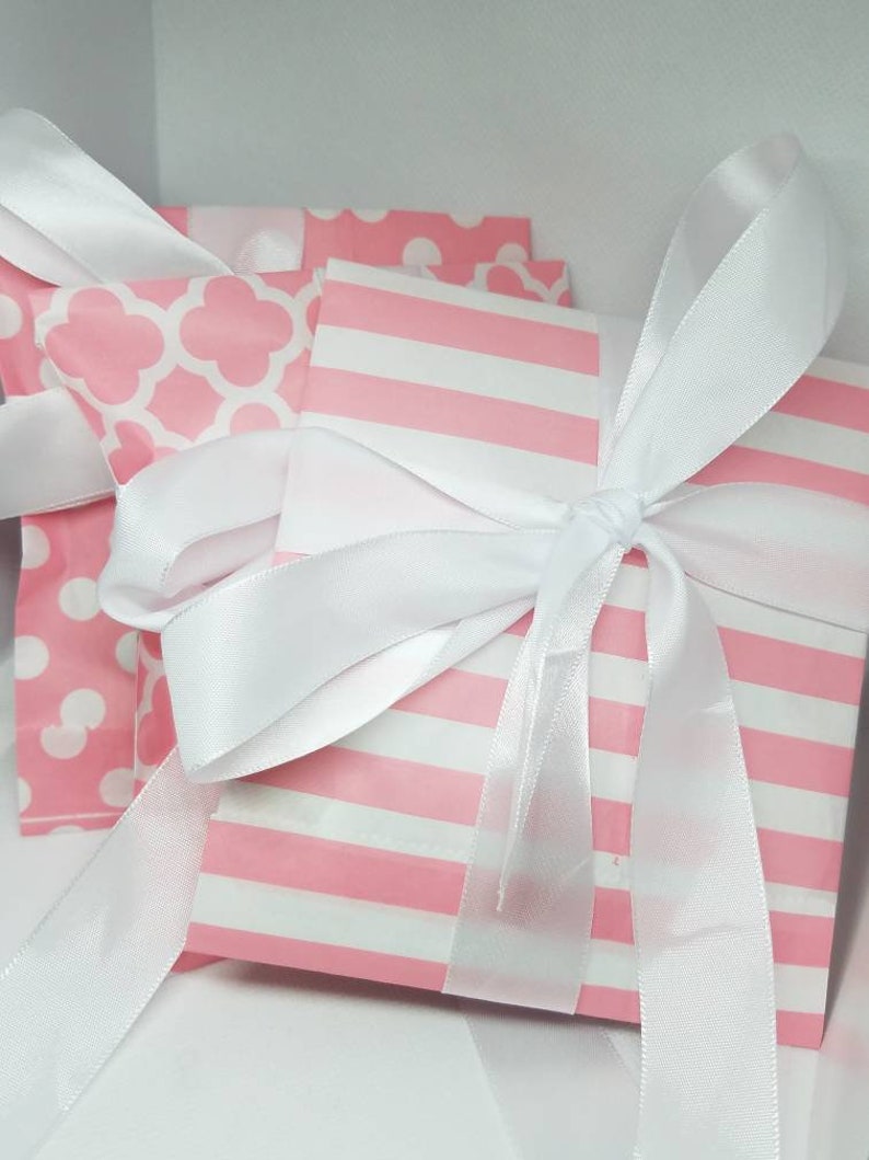 Puede incluir: Dos bolsas de regalo rosas con lunares blancos y un patr&oacute;n geom&eacute;trico blanco. Las bolsas est&aacute;n atadas con una cinta de sat&eacute;n blanca.