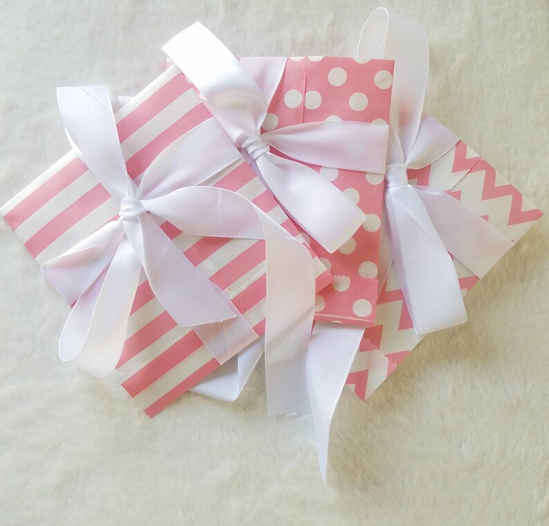 Puede incluir: Tres bolsas de regalo rosas con lunares blancos, rayas y un patr&oacute;n de chevron. Cada bolsa est&aacute; atada con una cinta de sat&eacute;n blanca.