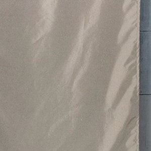 May include: A close-up of a smooth, off-white fabric with a subtle sheen. The fabric has a slight wrinkle in the center.