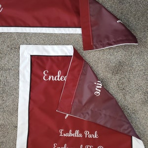 May include: Burgundy red fabric banner with white trim and white embroidered text. The text reads "Endeavoring" and "Isabella Park Englewood, FL".