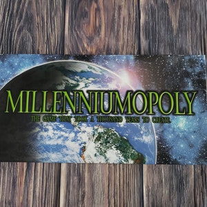 Puede incluir: Caja de juego de mesa "Millenniumopoly" con letras verdes y blancas. El fondo presenta una imagen azul y verde de la Tierra y un cielo estrellado. El texto "The game that took a thousand years to create" está debajo.