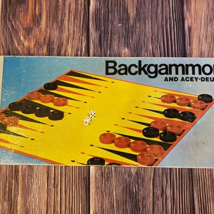 May include: A vintage Milton Bradley Backgammon and Acey-Deucy game box. The box is blue with a yellow and black backgammon board and red and black game pieces. The text on the box reads "Backgammon and Acey-Deucy".