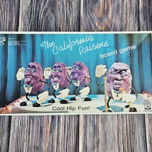 May include: A vintage board game box featuring the California Raisins. The box art shows four anthropomorphic raisin characters in suits, with the text "The California Raisins board game" and "Cool Hip Fun!" on a blue curtain backdrop.