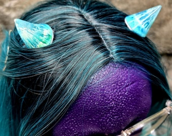 May include: A close-up of a purple head with teal hair and two small, translucent blue horns. The horns have a marbled effect with green and white accents. Clear-framed glasses are visible at the bottom of the image.