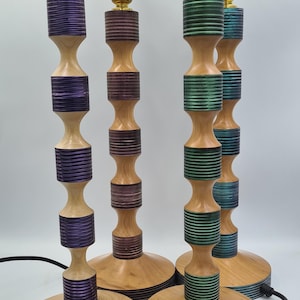 May include: Four wooden table lamps with different coloured wood grain patterns. The lamps have a brass base and a round wooden base.