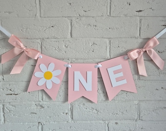 Op de afbeelding: Een roze slinger met drie wimpels aan een wit lint met lichtroze satijnen strikken aan de uiteinden. De eerste wimpel toont een witte margriet met een geel hart, de volgende twee wimpels tonen de witte letters N en E.