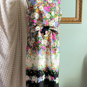 Puede incluir: Un vestido sin mangas con estampado floral en tonos rosa, morado, amarillo y verde. El vestido tiene una cinta negra atada a la cintura y un patr&oacute;n de rayas blancas y negras en la parte inferior.