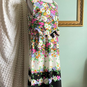 Puede incluir: Un vestido sin mangas con estampado floral en tonos rosa, verde, blanco y negro. El vestido tiene un corpi&ntilde;o ajustado y una falda fluida. El vestido est&aacute; en un maniqu&iacute;.