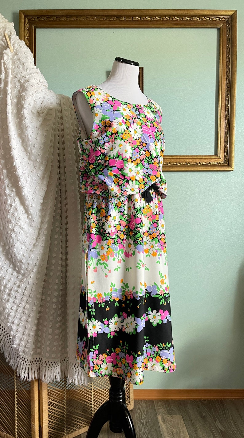 Puede incluir: Un vestido sin mangas con estampado floral en tonos rosa, verde, blanco y negro. El vestido tiene un corpi&ntilde;o ajustado y una falda fluida. El vestido est&aacute; en un maniqu&iacute;.