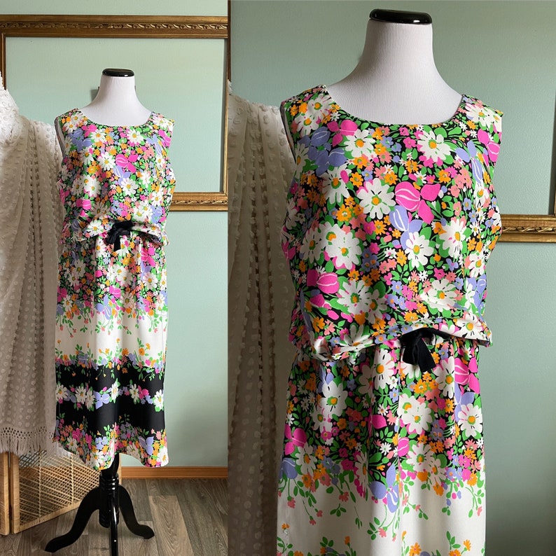 Puede incluir: Un vestido sin mangas con estampado floral en tonos rosa, blanco, naranja y verde. El vestido tiene una cinta negra en la cintura y un patr&oacute;n de rayas blancas y negras en el dobladillo.