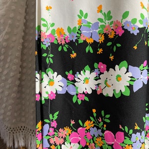 Puede incluir: Una tela negra y blanca con un patr&oacute;n floral. Las flores son rosas, naranjas, verdes y moradas. La tela tiene una costura blanca en el lateral.